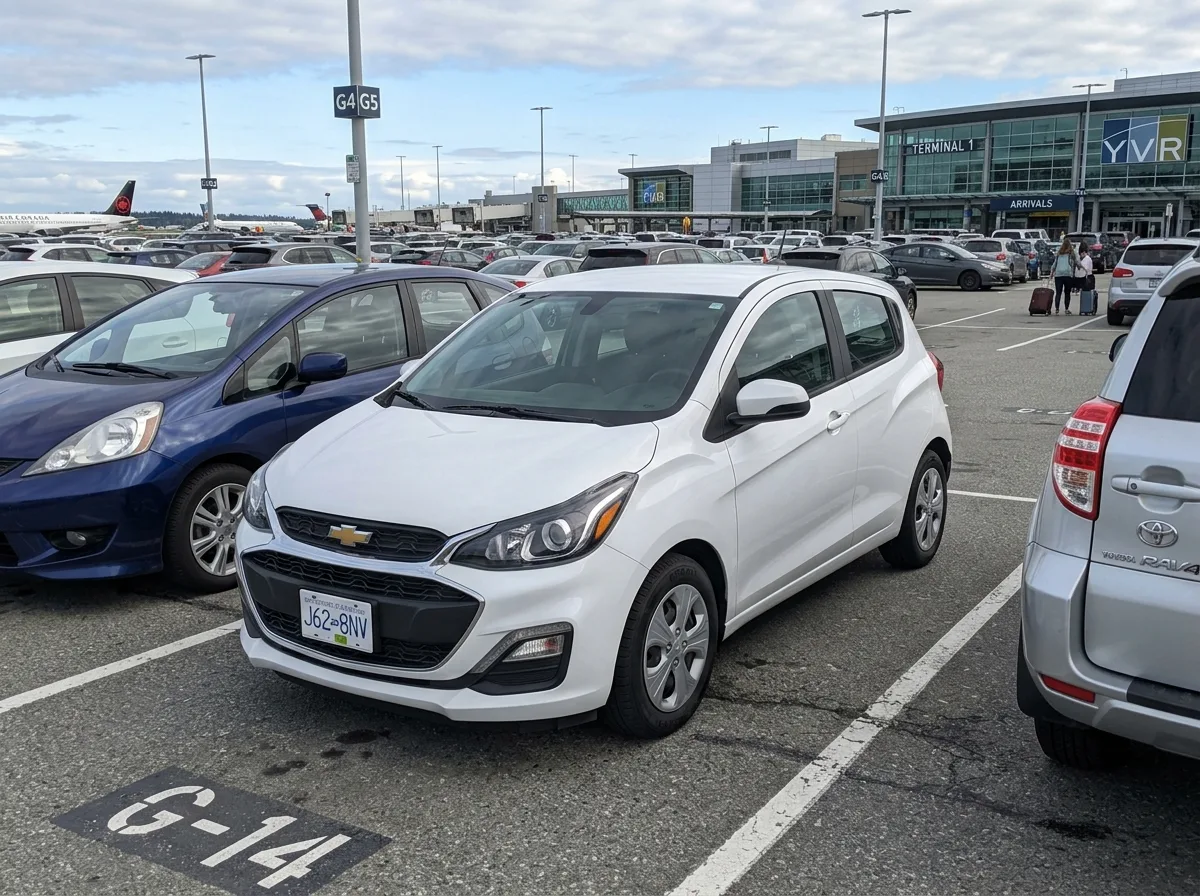 Chevrolet Spark economy hatchback in white, parked at airport lot, front three-quarter view